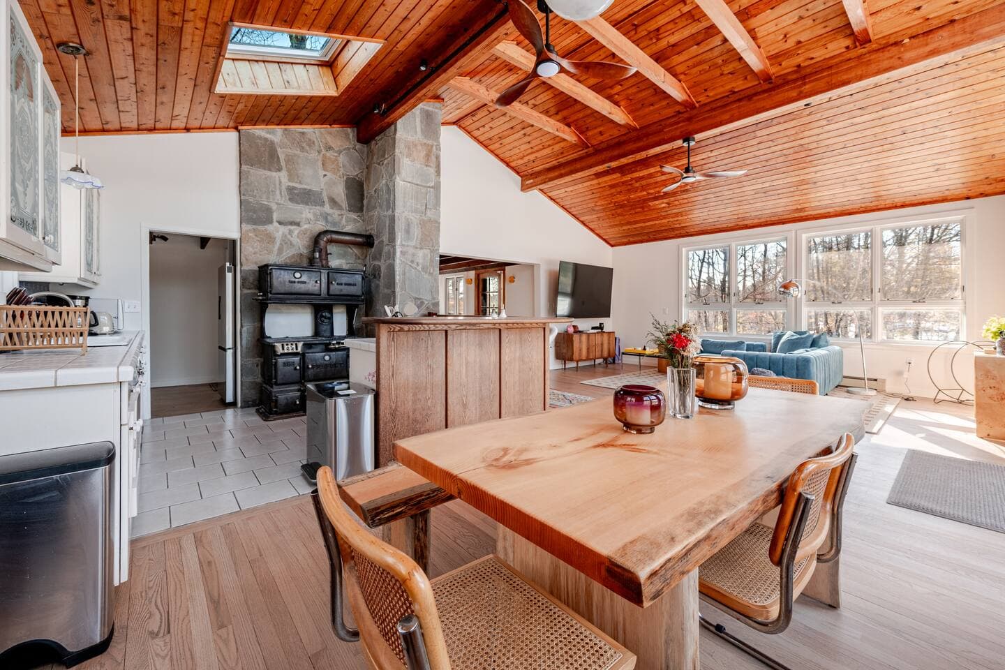 Open kitchen and dining area with stone wood stove and vaulted cedar ceiling at The Cedar Stock Cabin